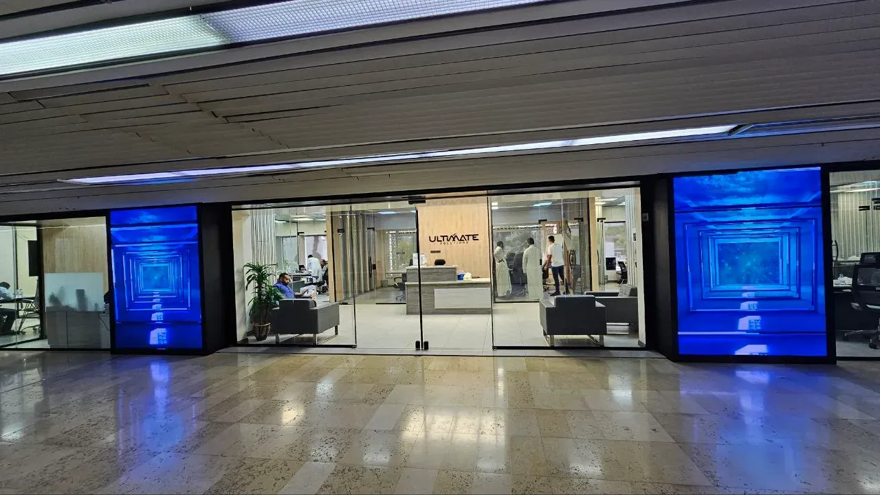 Pair of vertical Ruqaqa flat LED screens flanking a glass office storefront, showing immersive blue content