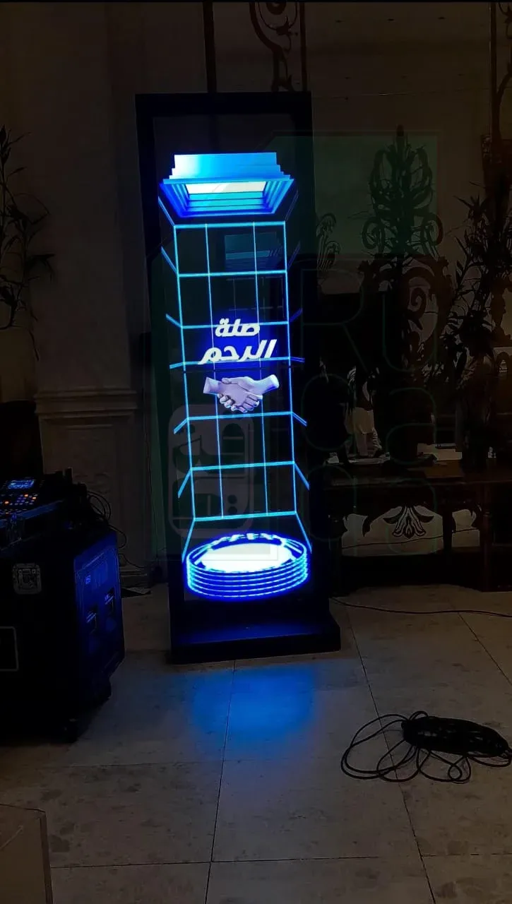 Ruqaqa freestanding transparent OLED screen with a black frame on a base, content and a handshake graphic floating on clear glass while the plants and room behind stay visible